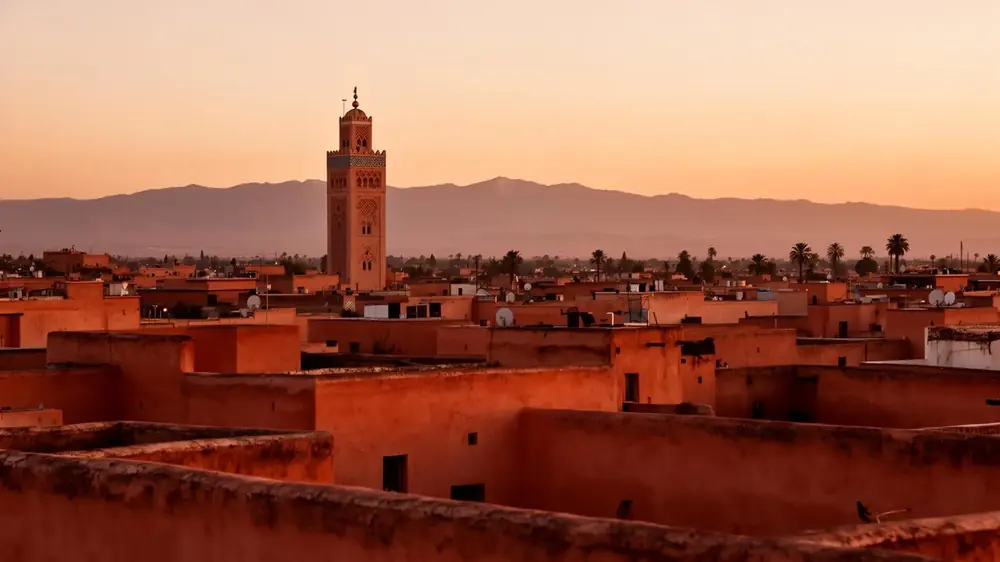 Vue panoramique des toits ocre de la médina de Marrakech au coucher du soleil avec le minaret de la Koutoubia et l'Atlas en arrière-plan